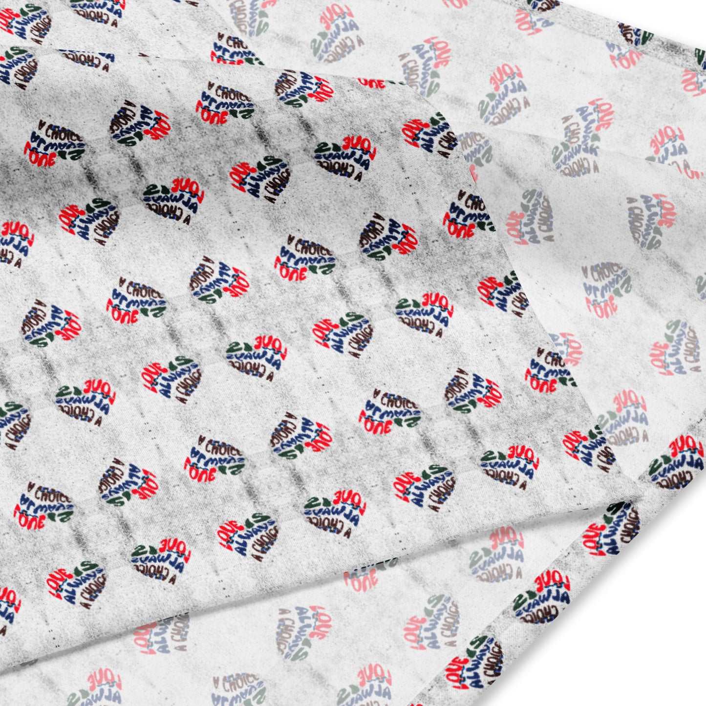 Close-up of a white all-over print fabric featuring small heart shapes with the phrase Love Is Always A Choice Bandana in red, blue, and black lettering arranged in a repeating pattern.
