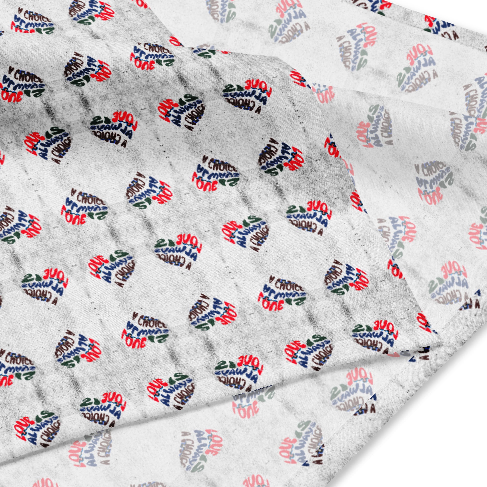 Close-up of a white fabric bandana with an all-over print of small hearts featuring the phrase Love Is Always A Choice Bandana in red, black, and blue lettering.