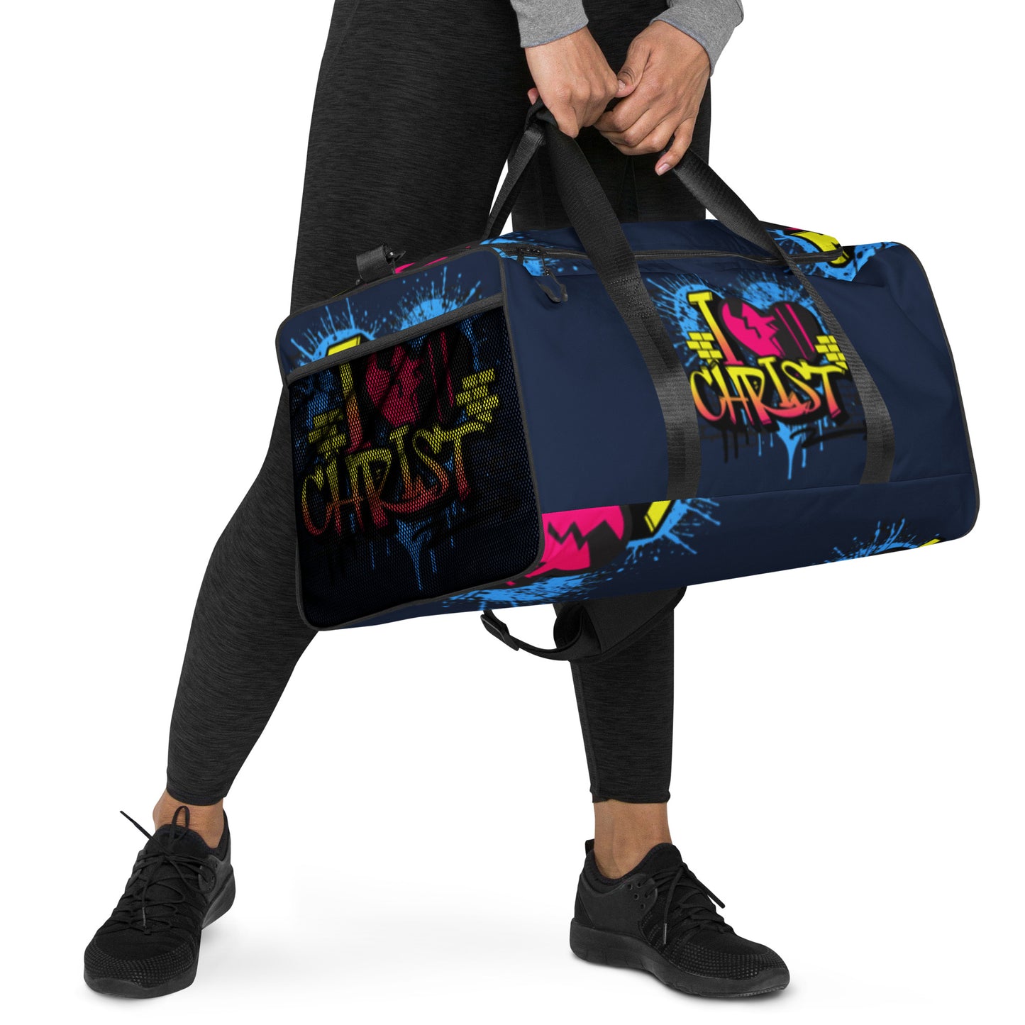 Person holding a navy blue Duffle Bag – I Love Christ with colorful graffiti-style faith-inspired design, paired with black athletic shoes and dark leggings, walking with purpose.