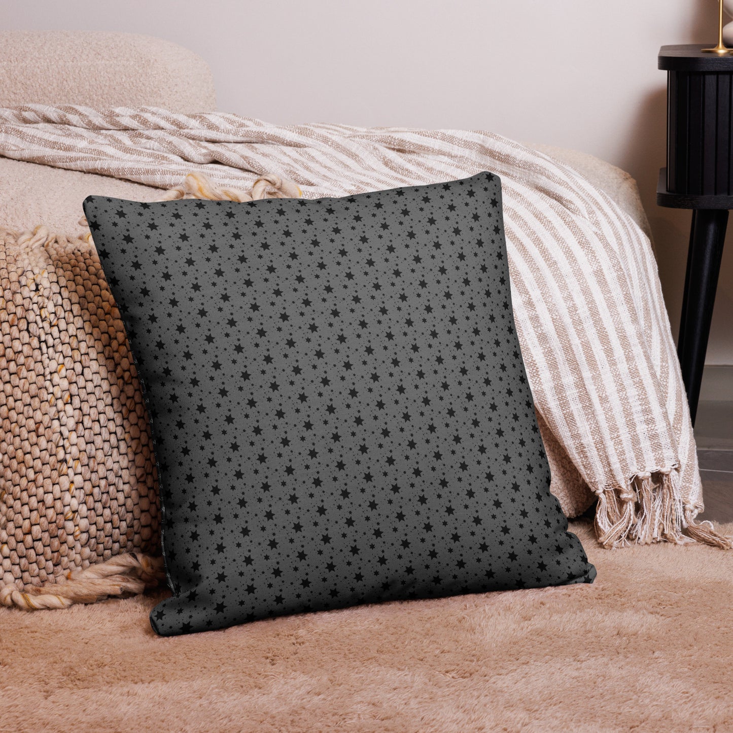 Moon Dreams Pillow featuring a dark fabric with a subtle all-over star pattern, placed on a cozy neutral-toned rug next to a textured knitted cushion and striped throw blanket.