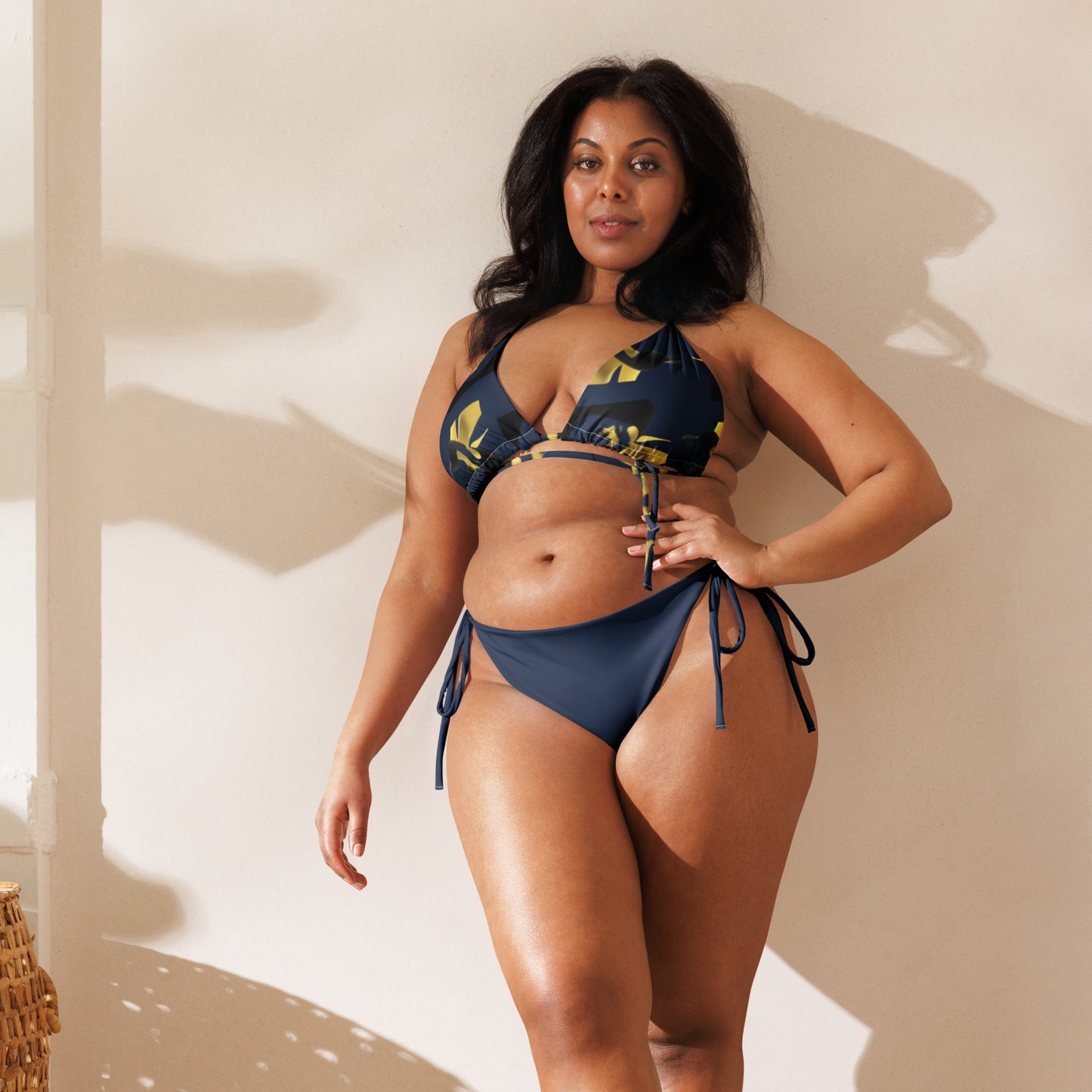 Woman modeling Spring Fling Navy & Yellow Recycled String Bikini with navy and yellow floral patterned top and solid navy tie-side bottoms against a neutral background.