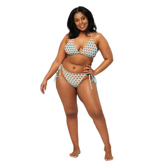 Confident plus-size woman wearing a Garden Teal Recycled String Bikini with teal and white pattern, posing barefoot with hand on hip and smiling.