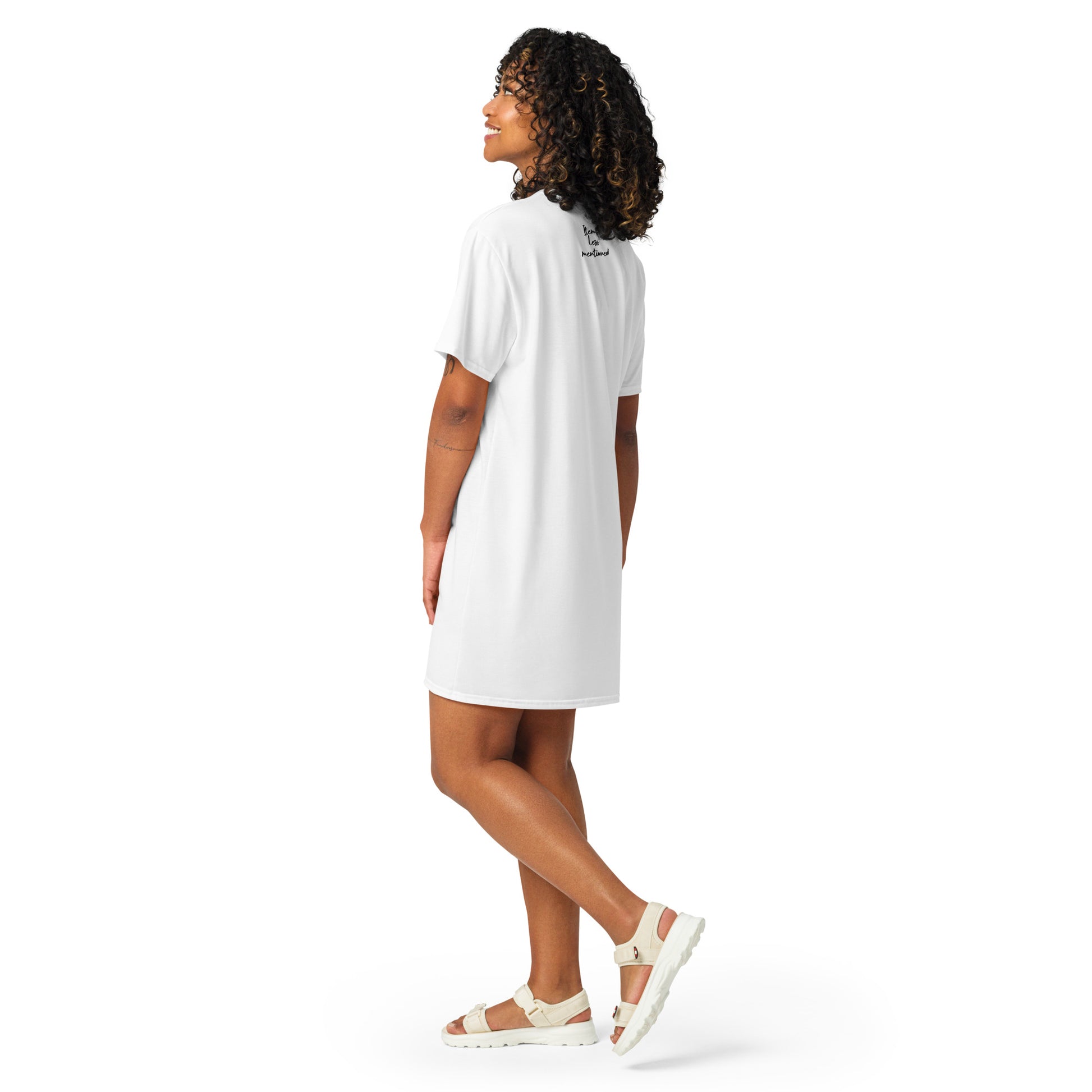 A woman wearing a white Peace on the Water T-Shirt Dress, standing in a relaxed pose with sandals, showcasing faith-inspired apparel featuring melanin-rich imagery and purpose-driven messaging.