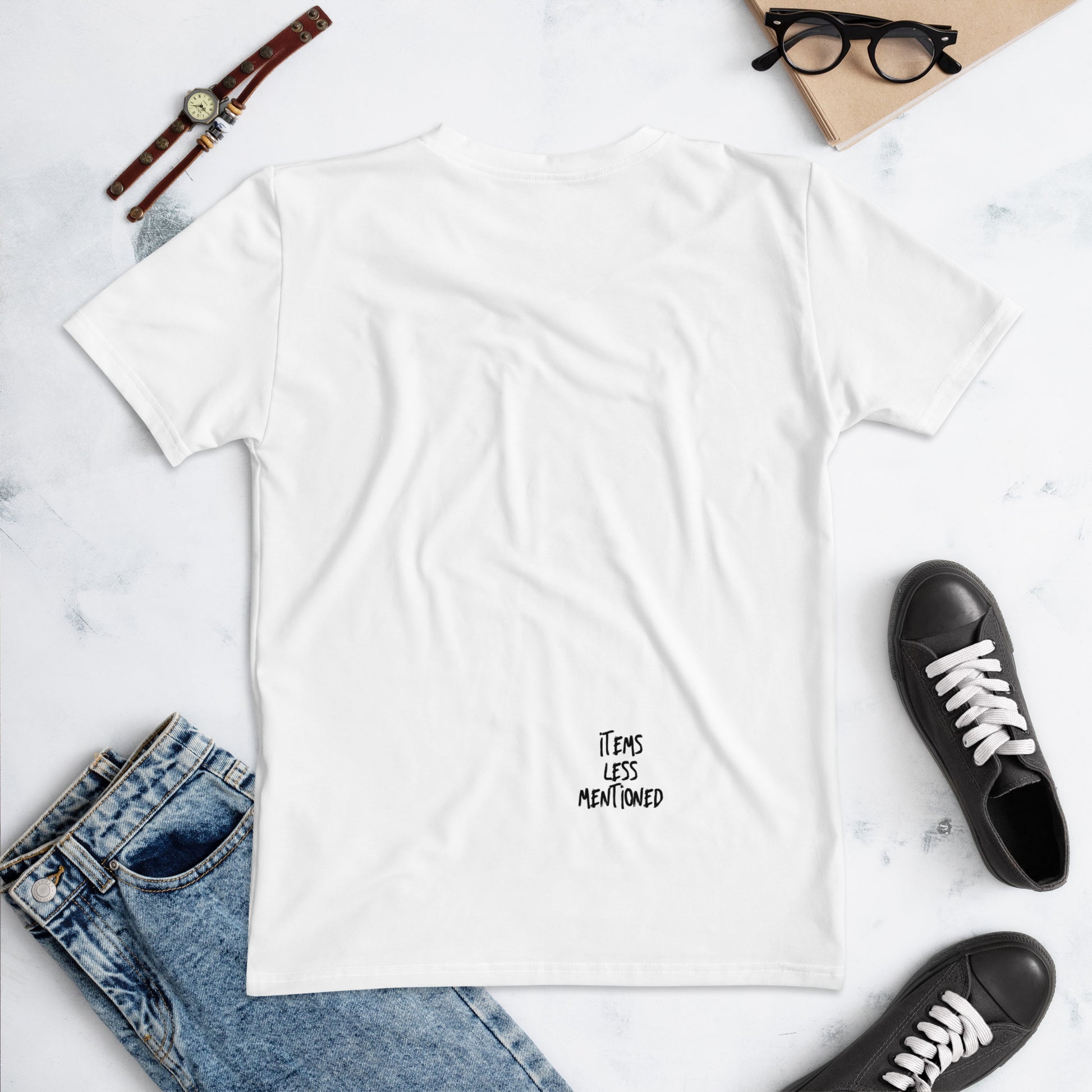 White Glam Squad Women's T-Shirt laid flat with a small "Items Less Mentioned" logo near the bottom, styled with casual blue jeans, a wristwatch, glasses, and black sneakers in the background.