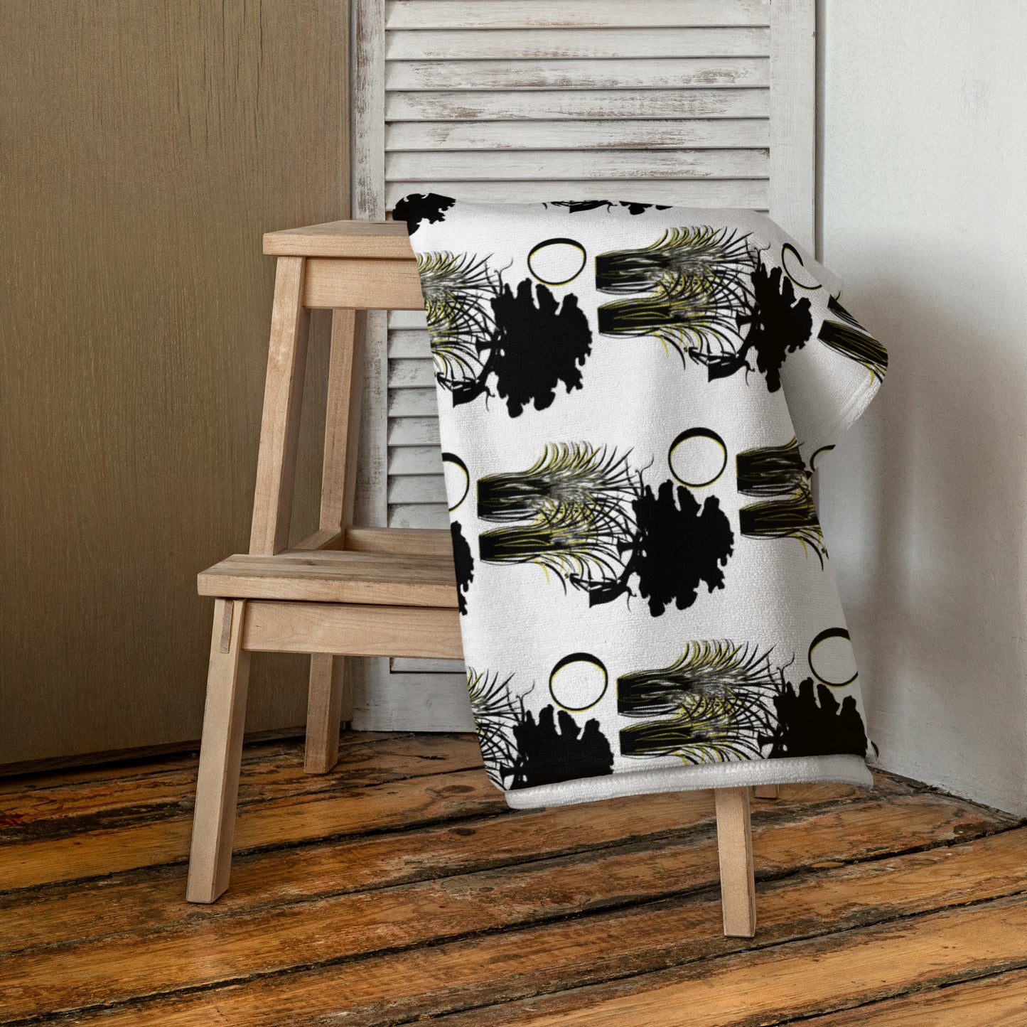 Moon & Wildgrass Towel draped over a wooden chair, featuring a white background with black silhouette trees and abstract gold accents, embodying faith-inspired and melanin-rich design.