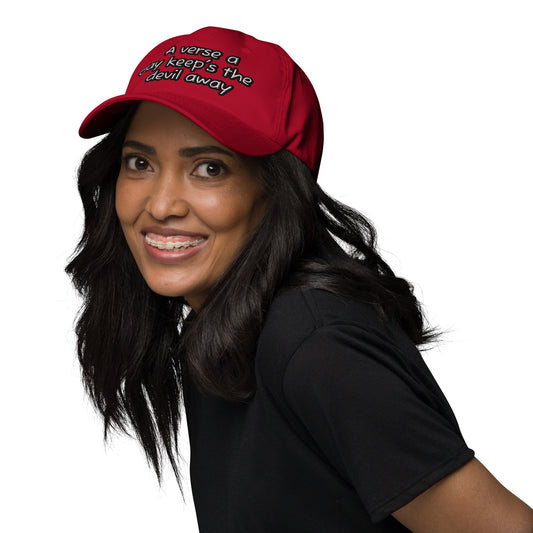 Smiling woman wearing a red Dad Hat – A Verse a Day Keeps the Devil Away with black text, styled with loose dark hair and a black shirt.