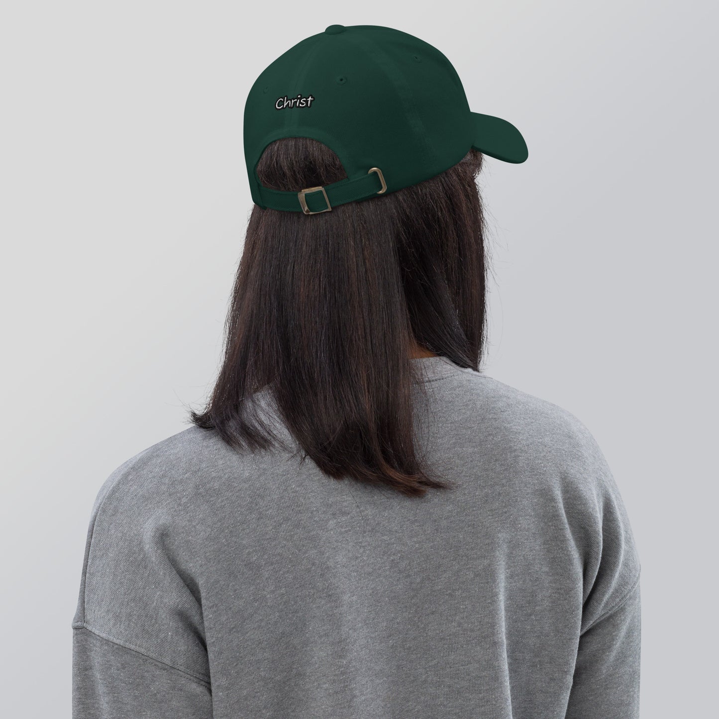 Person wearing a dark green Dad Hat – A Verse a Day Keeps the Devil Away with an adjustable strap and "Christ" embroidered on the back, paired with a gray sweatshirt.