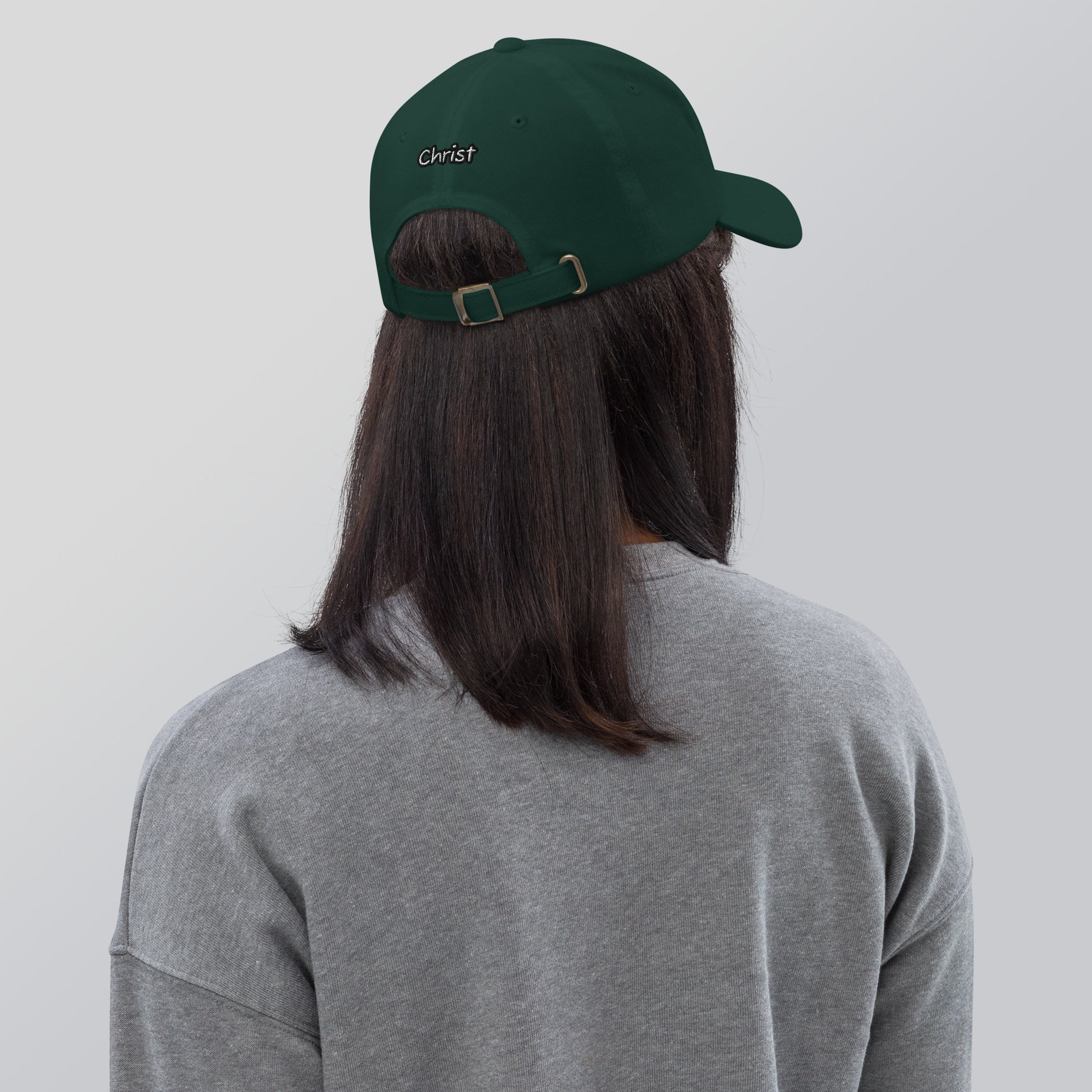 Person wearing a dark green Dad Hat – A Verse a Day Keeps the Devil Away with an adjustable strap and "Christ" embroidered on the back, paired with a gray sweatshirt.