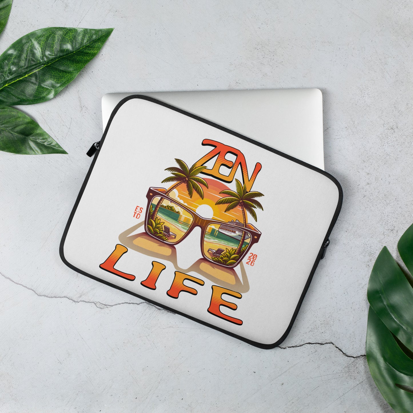 White Zen Life Laptop Sleeve featuring a colorful design of sunglasses reflecting a tropical sunset with palm trees, placed on a silver laptop on a light marble surface with green leaves nearby.