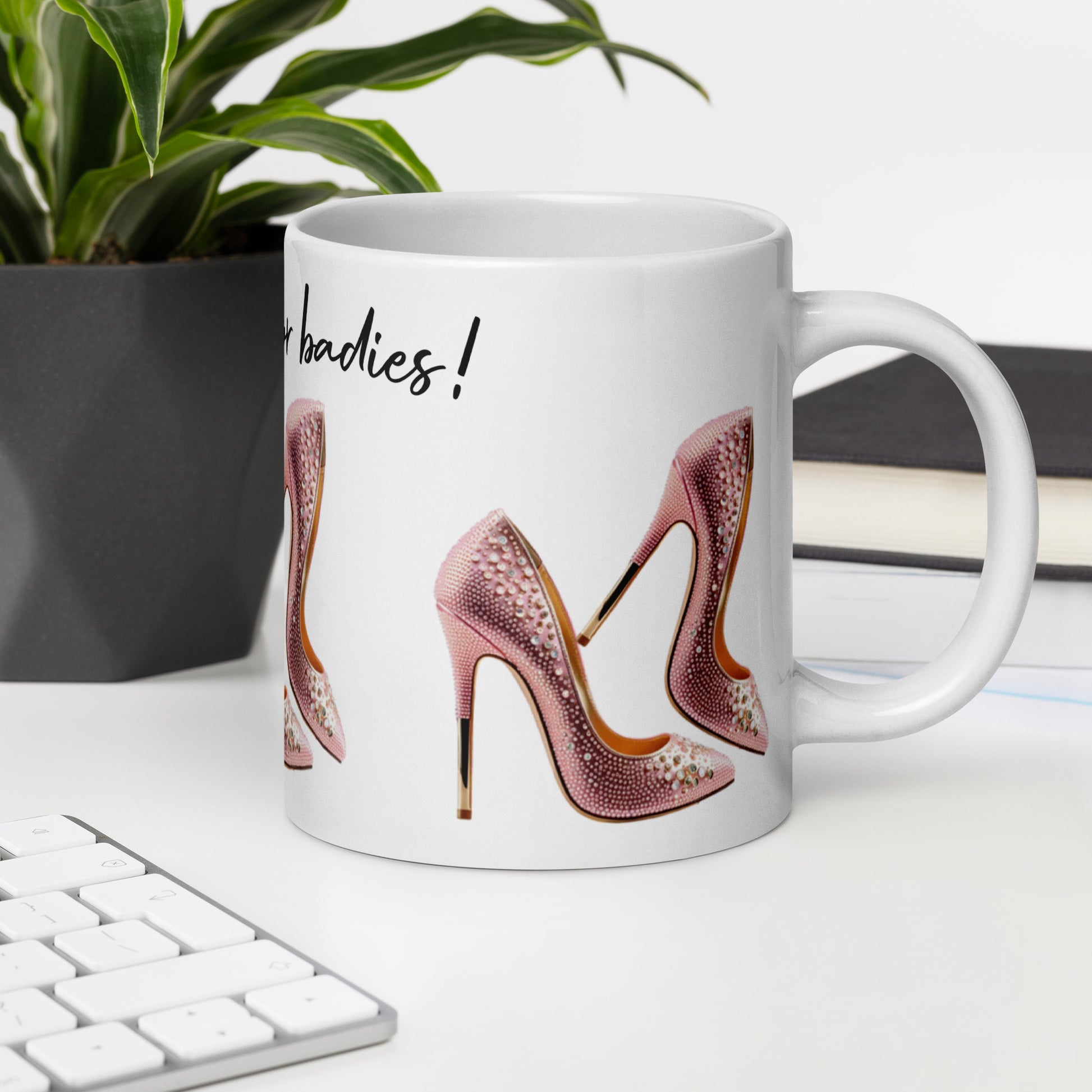 White glossy ceramic mug featuring pink high heels design and the text Mug – Life's Better in Pink Heels on a modern office desk with plant and keyboard, faith-inspired inspirational gift.